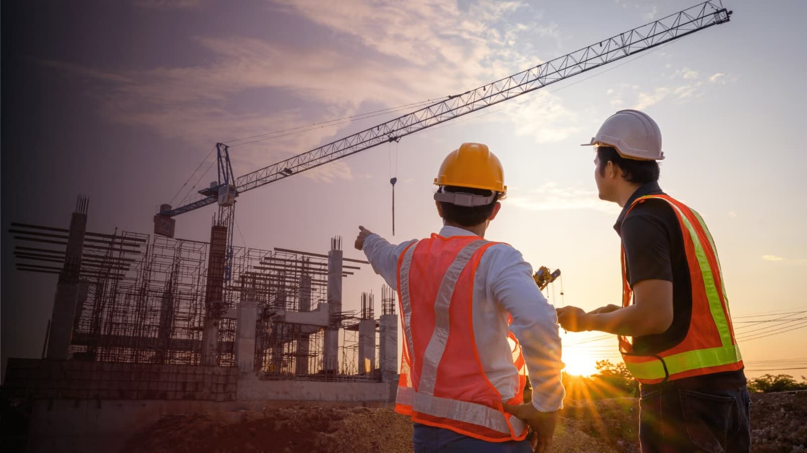 Two construction engineers in safety vests and hard hats at a build site at sunset